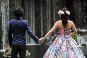 滝の前で手をつなぐ新郎新婦のフリー写真素材